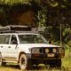A couple checking a road map on the hood of a black 4x4 Toyota Land Cruiser Prado rental vehicle in the rolling green hills of rural Rwanda, ideal for a self drive car hire in Rwanda road trip.