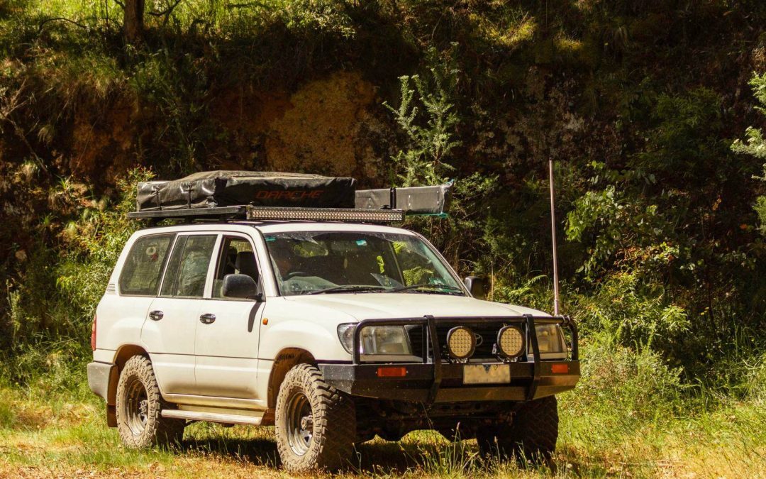 A couple checking a road map on the hood of a black 4x4 Toyota Land Cruiser Prado rental vehicle in the rolling green hills of rural Rwanda, ideal for a self drive car hire in Rwanda road trip.